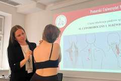 W sali warsztatowej na tle ekranu z prezentacją dwie kobiety podczas pokazu masażu