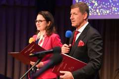 Dwie osoby stoją na scenie przed dużym ekranem 