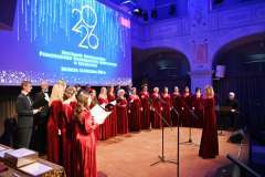 Chór w bordowych strojach śpiewa na scenie podczas Spotkania Noworocznego