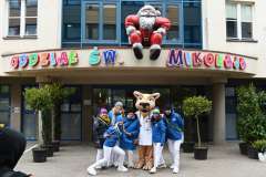 Maskotka pumy i uśmiechnięci młodzi ludzie przed wejściem do szpitala dziecięcego