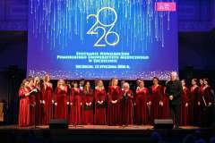 Chór w bordowych strojach śpiewa na scenie podczas Spotkania Noworocznego