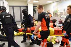 funkcjonariusze policji oraz ratownicy medyczni wynoszący z pomieszczenia ranną osobę na noszach