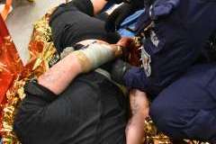 funkcjonariusz policji zakłuwający w kajdanki mężczyznę leżącego na podłodze, w tle leży ranna osoba