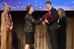 Kobieta i mężczyzna podają sobie ręce na scenie podczas uroczystej ceremonii.