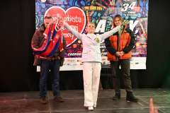 Jedna kobieta i dwóch mężczyzn stoi na scenie WOŚP, kobieta unosi ręce do góry