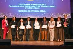 Grupa osób stoi na scenie z wyróżnieniami w ramkach, pozując do zdjęcia podczas uroczystego wydarzenia