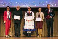 Grupa osób stoi na scenie z wyróżnieniami w ramkach, pozując do zdjęcia podczas uroczystego wydarzenia