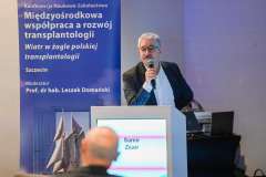 Mężczyzna przemawia przy mównicy podczas konferencji; obok widoczny baner z tytułem wydarzenia dotyczącym współpracy w transplantologii