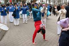Młody człowiek wykonuje przewrót na rękach podczas wydarzenia plenerowego, w tle orkiestra bębniarska i uczestnicy