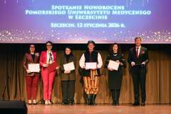 Grupa osób stoi na scenie z wyróżnieniami w ramkach, pozując do zdjęcia podczas uroczystego wydarzenia