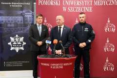 Trzech mężczyzn stoi przy mównicy. Jeden przemawia