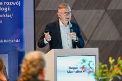 Mężczyzna przemawia przy mównicy podczas konferencji; obok widoczny baner z tytułem wydarzenia dotyczącym współpracy w transplantologii