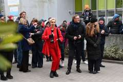 Kobieta w czerwonym stroju tańczy przed grupą osób przed szpitalem podczas wydarzenia 