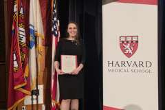 kobieta stojąca przed ścianką promocyjną , trzyma w ręku dyplom