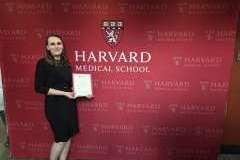 kobieta stojąca przed ścianką promocyjną , trzyma w ręku dyplom