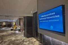 hol miejsca konferencyjnego, na ścianie monitor wyświetlający nazwę konferencji