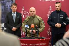 Trzech mężczyzn stoi przy mównicy. Jeden przemawia