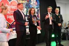 Trzech mężczyzn i dwie kobiety stoją na scenie Wośp, jeden mężczyzna mówi przez mikrofon