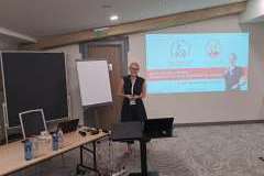 Kobieta stojąca w sali wykładowej przed ekranem rzutnika z wyświetloną prezentacją