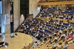 Prelegent stoi na scenie i prezentuje slajdy przed uczestnikami zjazdu