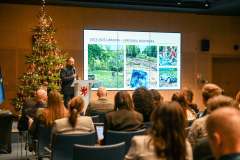 uczestnicy konferencji słuchają mężczyzny stojącego na scenie, w tle ekran wyświetlający prezentację