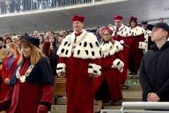 Grupa rektorów w czerwonych togach z futrzanymi kołnierzami i łańcuchami rektorskimi schodzi po schodach podczas uroczystości plenerowej