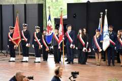 Poczet sztandarowy złożony z młodych osób w galowych mundurach stoi na scenie, trzymając sztandary uczelni i instytucji