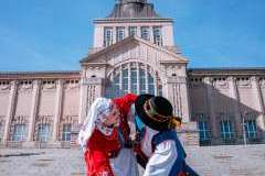 Para w tradycyjnych polskich strojach ludowych tańczy na tle monumentalnego gmachu z szerokimi schodami.