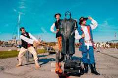 Trzech mężczyzn w strojach ludowych przy pomniku 