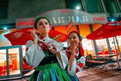 Dwie panie w strojach ludowych stoją przed restauracją Bar Rab. Jedna zakryła usta ręką, druga je kebaba. 