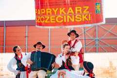 Dwie panie i trzech panów w strojach ludowych siedzą przed pomnikiem przedstawiającym puszkę szczecińskiego paprykarza. 