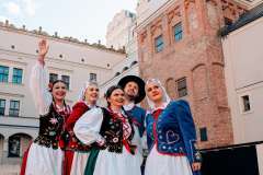 Cztery panie i jeden pan w strojach ludowych, stoją na dziedzińcu Zamku Książąt Pomorskich. Jedna pani wskazuje na coś palcem.