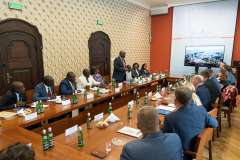 Grupa osób siedząca przy stole słucha jednego z uczestników spotkania