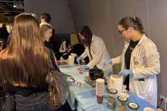 cztery młode kobiety rozmawiają przy stoisku promocyjnym, dwie ubrane są w uniformy lekarskie