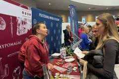 trzy kobiet rozmawiają przy stoisku promocyjnym uczelni