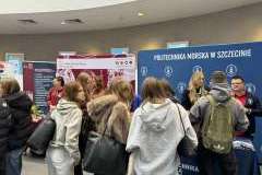młodzi ludzie w sali ze stoiskami promocyjnymi uczelni