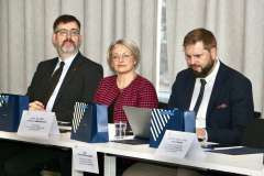 jedna kobieta i dwóch mężczyzn siedzą przy stole, na którym leżą dokumenty