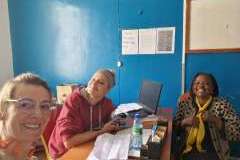 trzy kobiety siedzą przy biurku i uśmiechają się