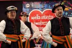 Mężczyźni w strojach ludowych występują na scenie podczas wydarzenia WOŚP.