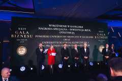 Wręczenie nagrody na scenie podczas XXIV Gali Biznesu w Szczecinie, z grupą laureatów i organizatorów stojących przed ekranem z nazwą wydarzenia