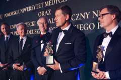 Laureaci w smokingach stoją na scenie podczas Gali Biznesu, trzymając statuetki i pozując do zdjęcia na tle ekranu z nazwą wydarzenia.