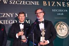 Dwóch mężczyzn w smokingach stoi na scenie Gali Biznesu w Szczecinie, trzymając statuetki i pozując do zdjęcia.