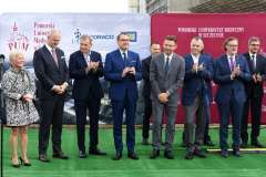 grupa osób stojących na tle ścianek z logotypami, niektórzy klaszczą