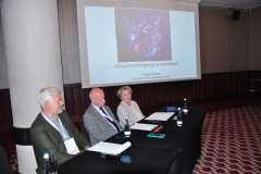 Trzy osoby siedzą przy stole prezydialnym podczas konferencji; w tle slajd z tytułem Sztuczna inteligencja w kardiologii