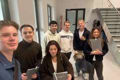 grupa młodych osób stojących na korytarzu i uśmiechających się do obiektywu aparatu. w tle schody