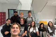 grupa młodych osób stojących na korytarzu i uśmiechających się do obiektywu aparatu. w tle schody