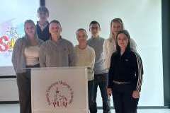 grupa młodych osób stoją przy mównicy i uśmiechają się do obiektywu aparatu