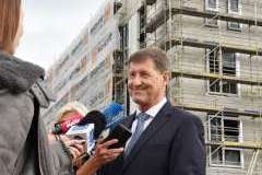 mężczyzna udzielający wywiadu, w tle zawieszona wiecha na budynku