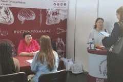 Rozmowy z zainteresowanymi osobami podczas targów. W tle ścianka uczelni z medycznymi motywami w kolorze bordo