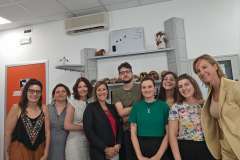 Grupa dziewięciu osób, kobiet i mężczyzna, stoi razem w sali uniwersyteckiej, uśmiechając się do kamery.